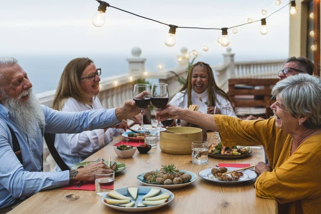 Senior friends enjoying red wine and Mediterranean food during dinner by the sea.