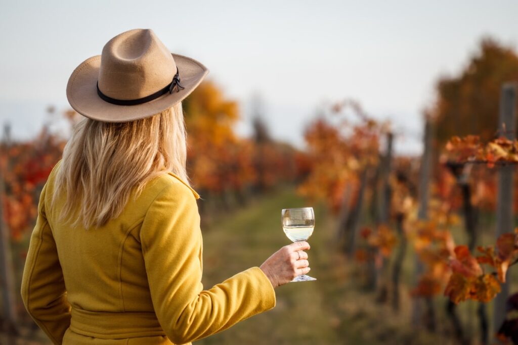 Woman standing in a vineyard during fall holding a glass of white wine.