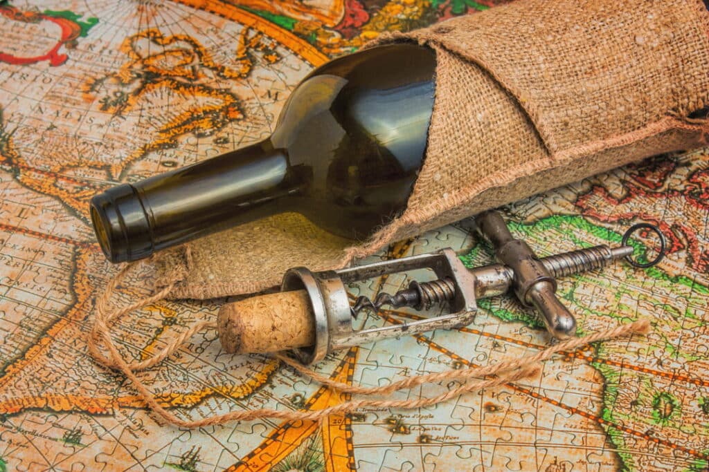 Bottle of wine and corkscrew placed on a world map symbolizing a wine tasting trip.