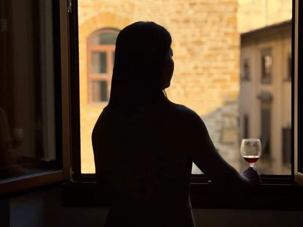 A woman holds a glass of red wine looking out a window over the stone buildings of Florence, Tuscany, Italy